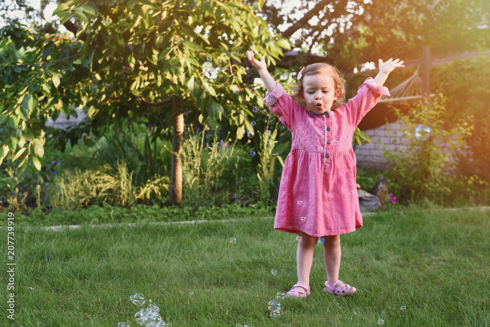 happy little girl in pink dress at green garden with flying soap bubbles happy little girl in pink dress at green garden with flying soap bubbles