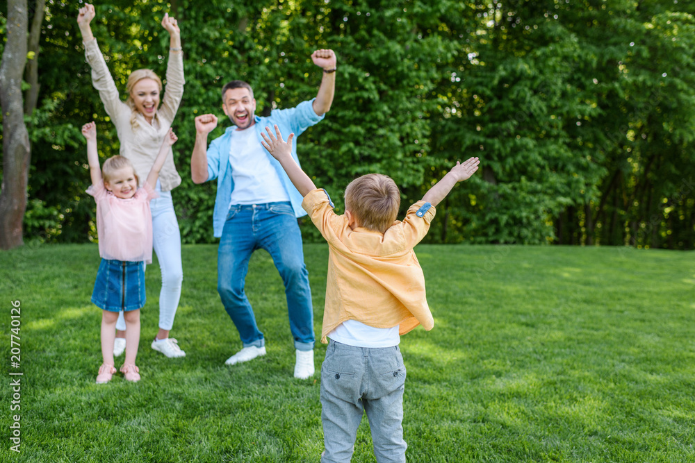 Obraz premium cheerful family raising hands and smiling each other in park