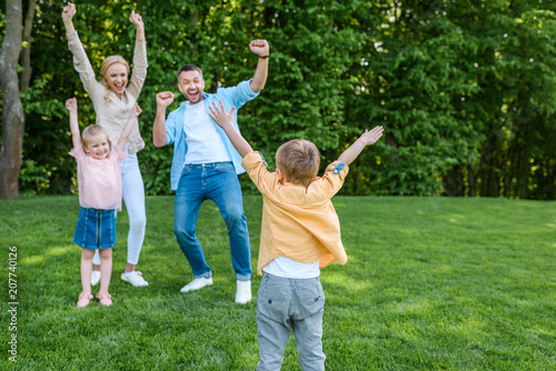 cheerful family raising hands and smiling each other in park