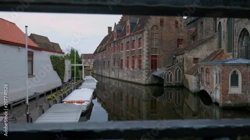 Camera rises past love locks on railings to reveal Sint-Janshospitaal and Dijver Canal in Brugge Belgium  photo