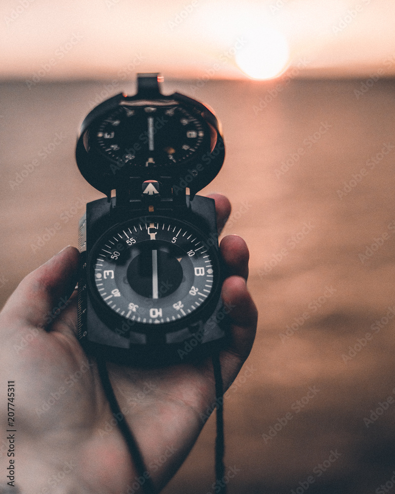 Closeup of male hand holding compass on sunset background Closeup of male hand holding compass on sunset background