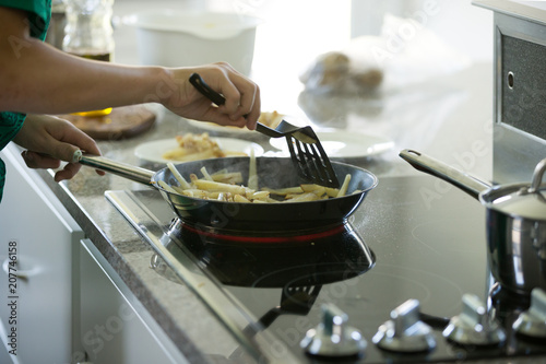 Closeup of boy's hands frying potatoes on a pan in the kinchen.