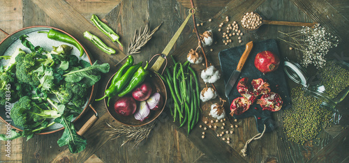 Winter vegetarian, vegan food cooking ingredients. Flat-lay of seasonal vegetables, fruit, beans, cereals, kitchen utencils, dried flowers, olive oil over wooden background, top view, wide composition