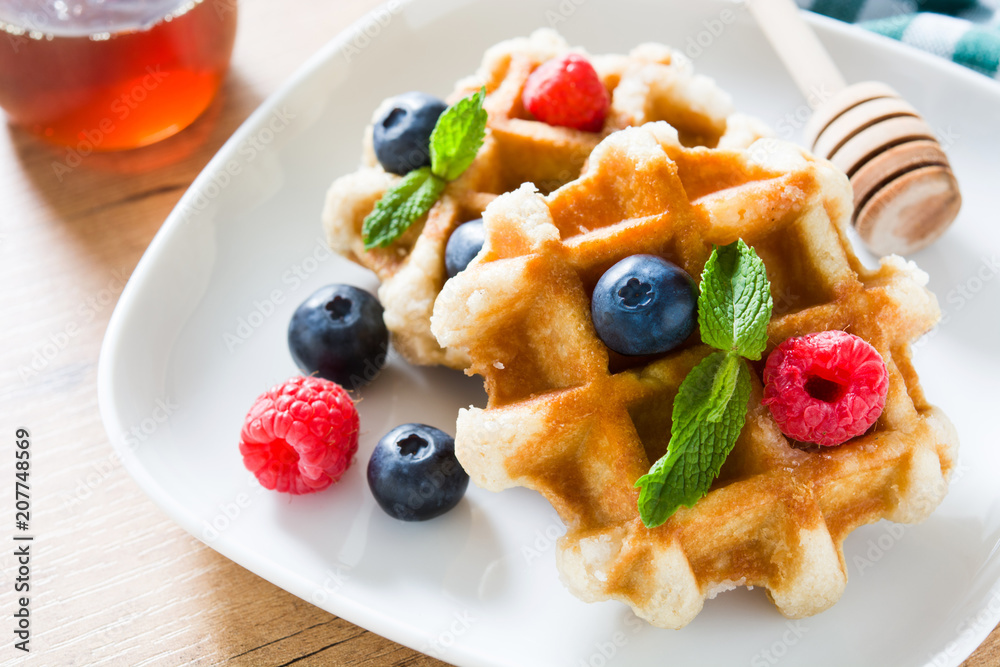 Traditional belgian waffles with blueberries and raspberries on wooden table Traditional belgian waffles with blueberries and raspberries on wooden table