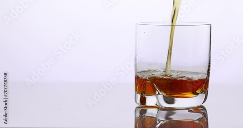 whisky pouring in a glass on a white reflective surface