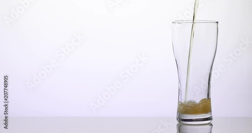 Beer pouring in a glass on a white reflective surface