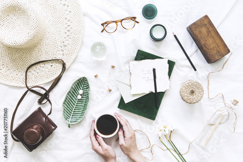 Trendy and stylish flat lay with woman hands on cup of coffee, accessories, hat, glasses, letters and notebook. Lifestyle and blogger concept.