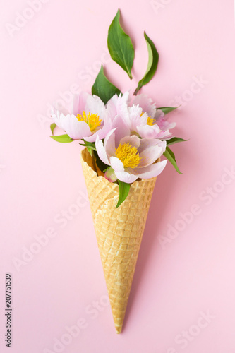 Spring or summer mood concept. Flat-lay of waffle sweet cone with peonies over pastel light pink background, top view.