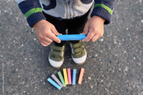 Baby's hands holding colorful blue chalk closeup. Children's Creativity. Early child development,top view.The boy's legs, sneakers, asphalt, multicolored chalks, soft focus.
