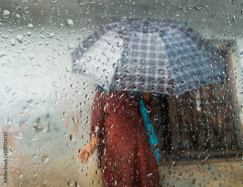 Monsoon season in Kathmandu, Nepal. Woman holding an umbrella seen through a window. Focus on droplets on glass.