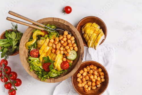Grilled chicken salad with vegetables and chickpeas in a wooden bowl on a white background. Healthy balanced diet concept.