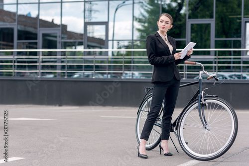 young businesswoman with digital tablet standing near retro bicycle on street