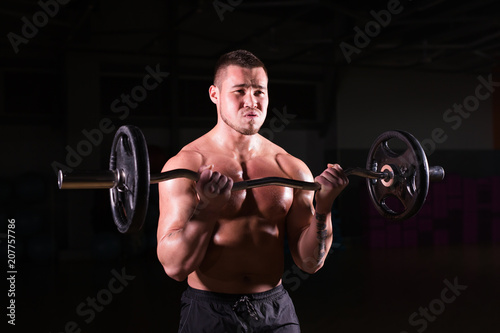 Muscular young man lifting weights on dark background