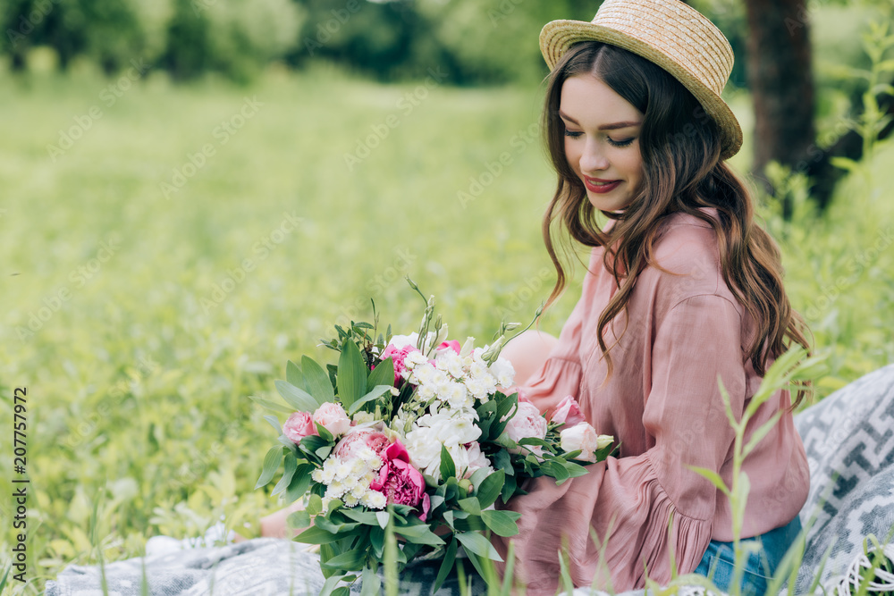 side view of beautiful smiling woman with bouquet of flowers resting on blanket in park