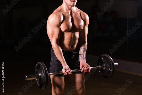 Muscular young man lifting weights on dark background