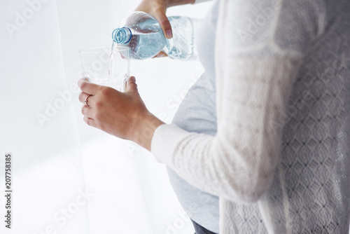 Unrecognizable pregnant woman pouring a glass of water