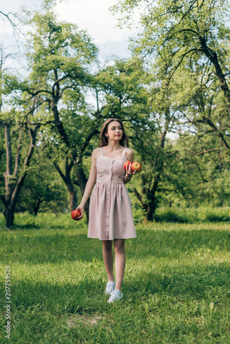 young woman in dress with ripe apples walking at countryside