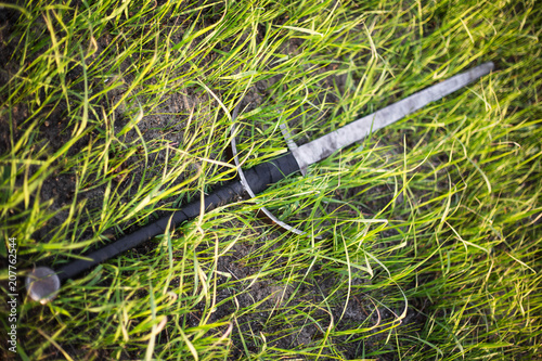 Fototapeta Naklejka Na Ścianę i Meble -  a two-handed sword lies in a tall green grass. The battlefield, after the battle. Crusade, medieval weapons. Lost, forgotten sword, fallen warrior.