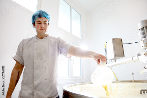 Cheese maker adding rennet to curdle cheese in vat
