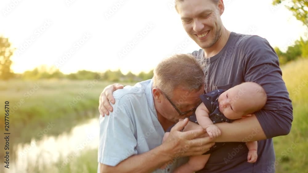Three generations of men. Grandpa, father and little grandson. Father and son greet each other with a handshake. Sunset, the bank of the river