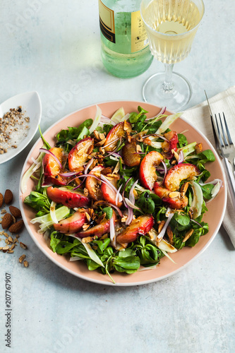 summer, very tasty salad with peaches, sweet onions and arugula with almonds on a table in a plate. simple healthy recipe and a bottle with a glass of white wine