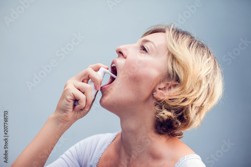 Spray for sore throat. Photo of a woman who treats her throat with a spray and sprinkles it in her mouth. The concept of health and disease.