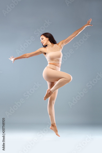 Attractive excited fitness girl, ballerina dancer in sportwear jumping of joy isolated over gray background. © Mike Orlov