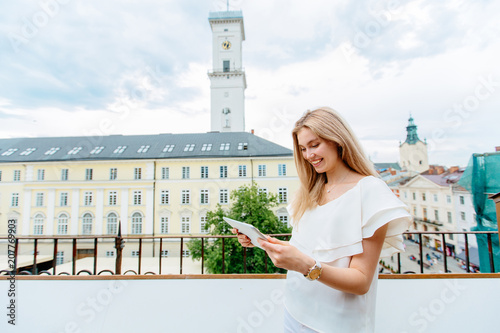Relaxed and cheerful. Work and vacation. Outdoor portrait of happy young woman using tablet computer on terrace with beautiful city view. © Iryna
