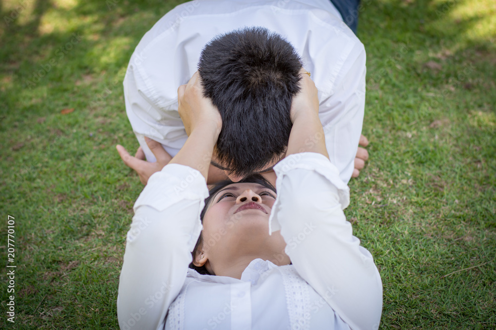 A pair of lovers in the park with man kissing young woman on the grass. A pair of lovers in the park with man kissing young woman on the grass.