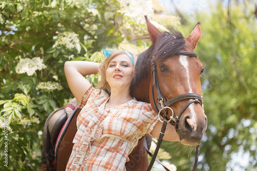 Cheerful, beautiful blonde girl walks in summer sunny weather in a forest by the river with a horse
