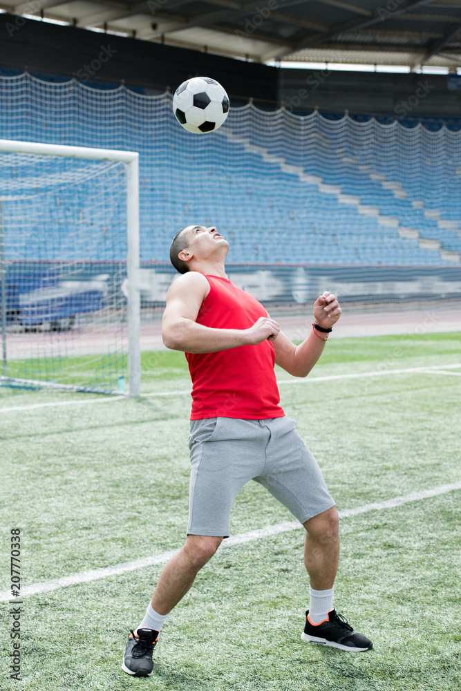 Full length portrait of handsome young man playing football in stadium, hitting ball with his head, copy space