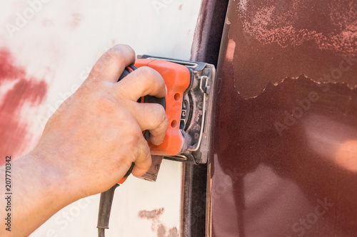 Male hand using a palm sander on a vehicle to remove paint photo