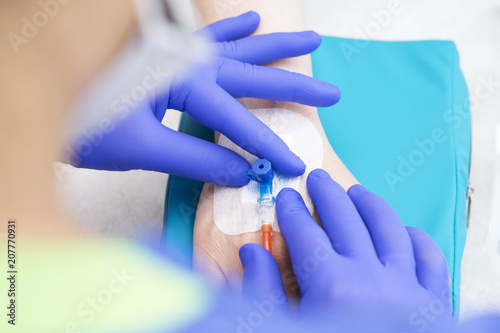 medical nurse with blue latex gloves inputs catheter to vein patient for drip of chemotherapy or another liquid medicine photo