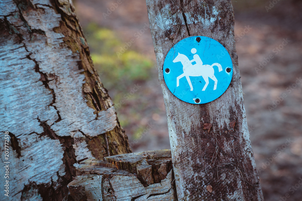 Fototapeta premium Bridle path round blue sign on a wooden stake, with blurry land path in the background. Germany