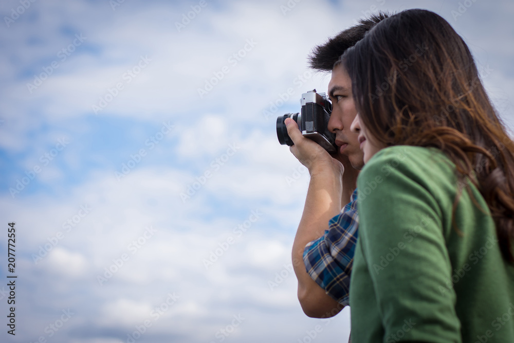 Young men and young women Couple together standing on bench waterfront port in the park. Handle vintage camera.