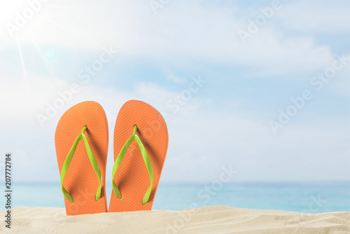 Pair of flip flops in sand on blue sky background
