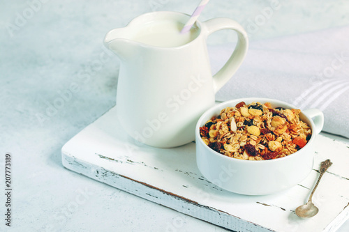 Cup of muesli with tropical fruits and white milk jug on wooden board. Concept of healthy eating in pure tones.