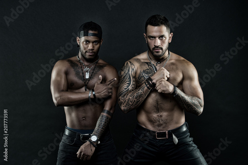 Athletes on confident faces with nude muscular chests and biceps. Machos with muscular tattooed torsos look attractive, dark background. Tattoo art concept. Guys sportsmen with sexy muscular torsos
