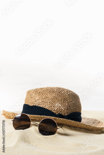 Straw hat and sunglasses in sand isolated on white