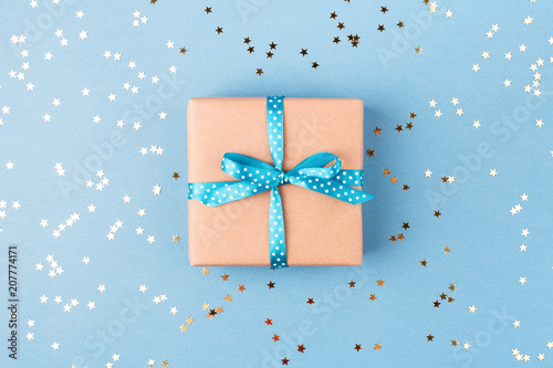 Gift box wrapped in kraft paper and tied with turquoise ribbon on blue backgr...