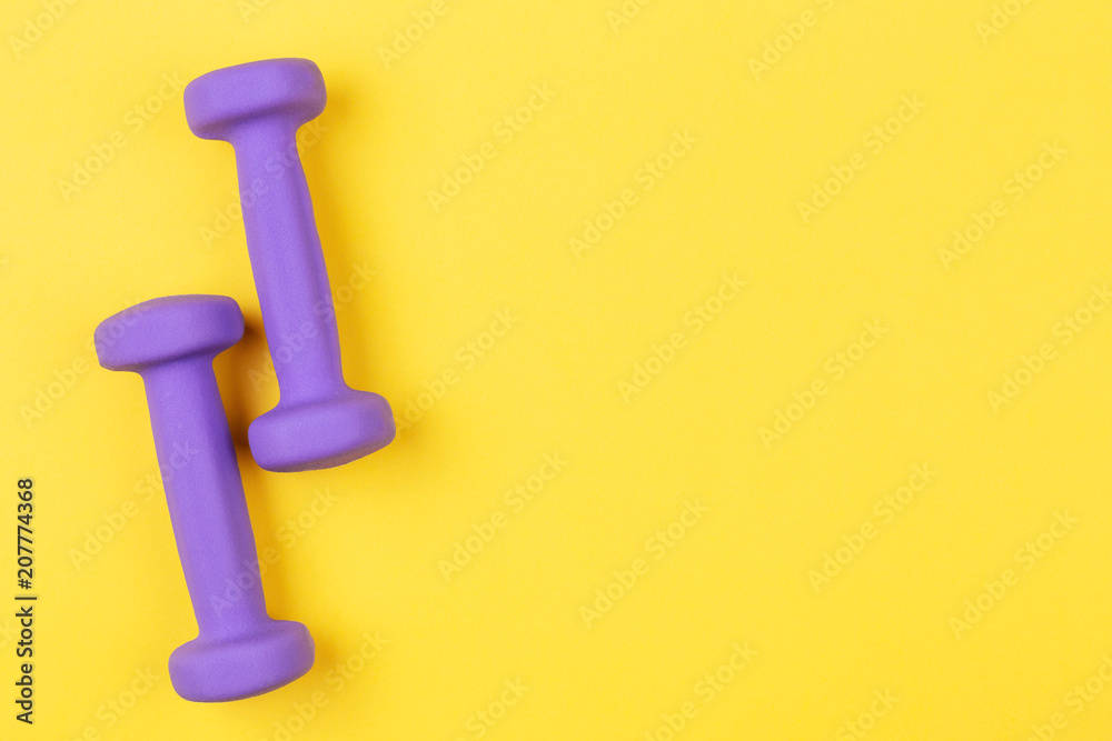 Two violet dumbbells on yellow background. Top view, copy space. Two violet dumbbells on yellow background. Top view, copy space.
