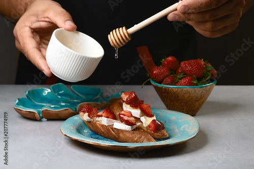 chef sprinkle the honey sweet sandwiches with strawberries, cheese, camembert, brie, nuts and honey on the whole grain bread bruschetta cooking by chef hand on light background photo