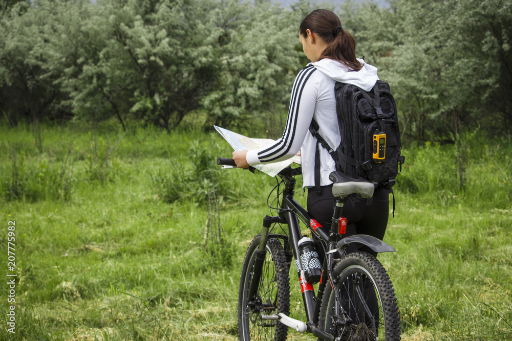 Obraz premium A young girl in a park stands with a bicycle and looks at the map