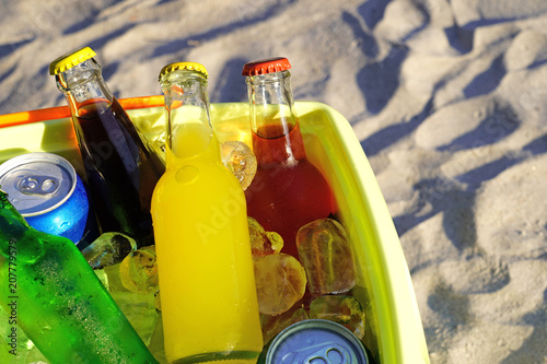 Colorful soda drinks and filled ice cubes in a coolbox on the beach sand.  photo