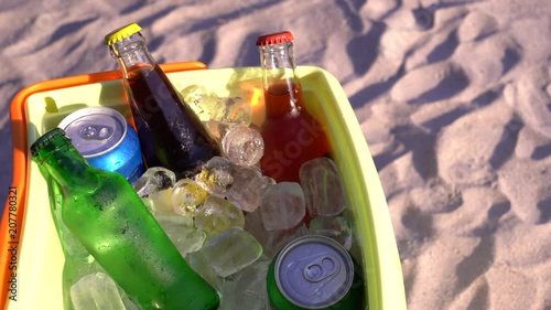 Colorful soda drinks and filled ice cubes in a coolbox on the beach sand. 4K video