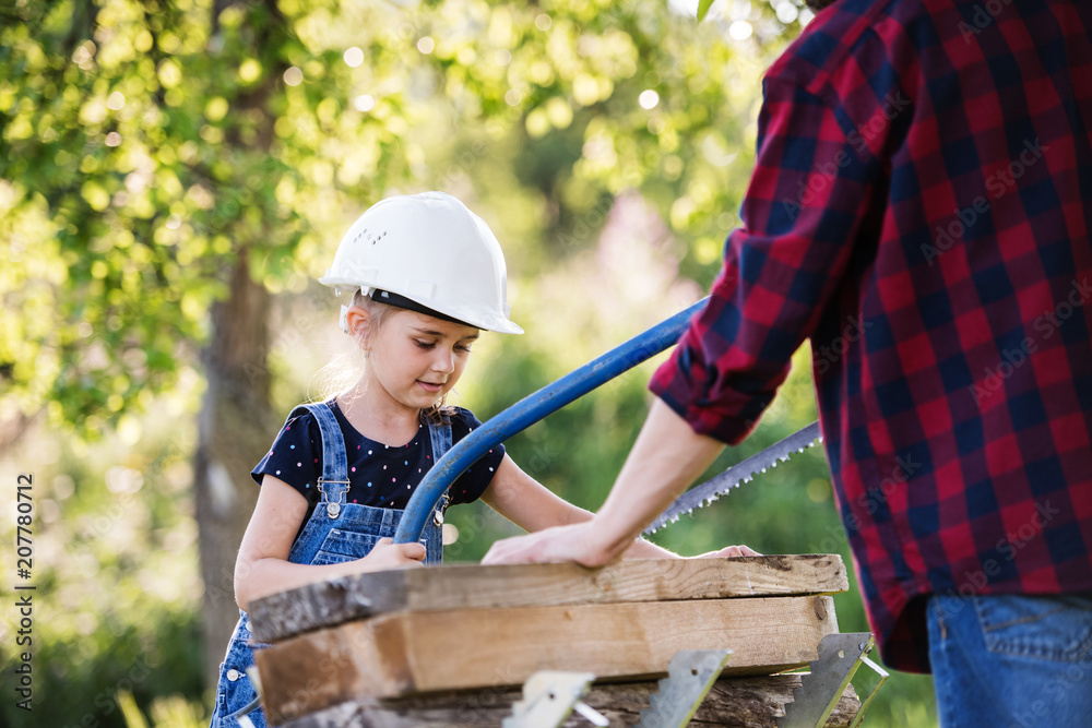 Father with a small daughter outside, making wooden birdhouse. Father with a small daughter outside, making wooden birdhouse.