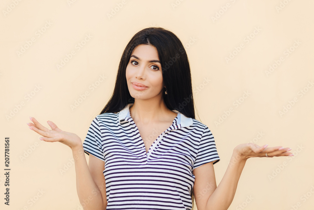 Shot of hesitant lovely female shrugs shoulders with puzzlement, doesn`t know answer on difficult question, poses against light pink background. Clueless brunette woman has doubtful expression Shot of hesitant lovely female shrugs shoulders with puzzlement, doesn`t know answer on difficult question, poses against light pink background. Clueless brunette woman has doubtful expression