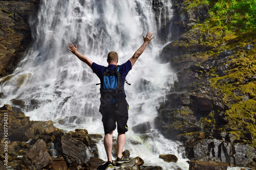 Hiker with backpack looking at waterfall in Norway. Concept of adventure and travel lifestyle. Point of destination. 
