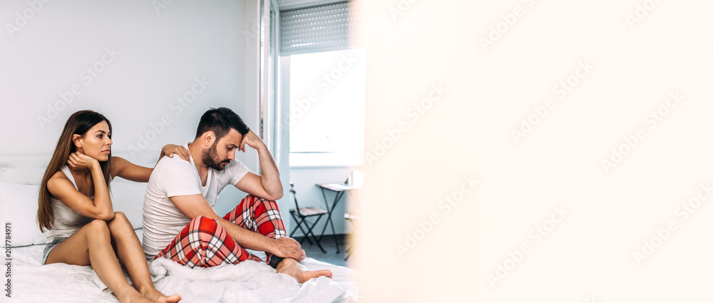 Sexual problems concept. Upset man sitting on the bed with woman comforting him. Sexual problems concept. Upset man sitting on the bed with woman comforting him.