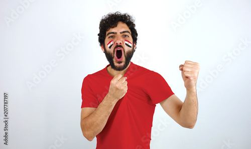 Sport fan screaming for the triumph of his team. Man with the flag of Egypt makeup on his face and red t-shirt.